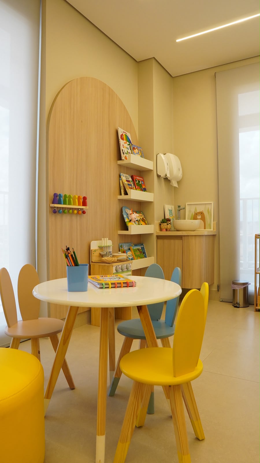 Cantinho infantil do consultório, com mesa e cadeiras em formato de coelhinho e estante de livros
