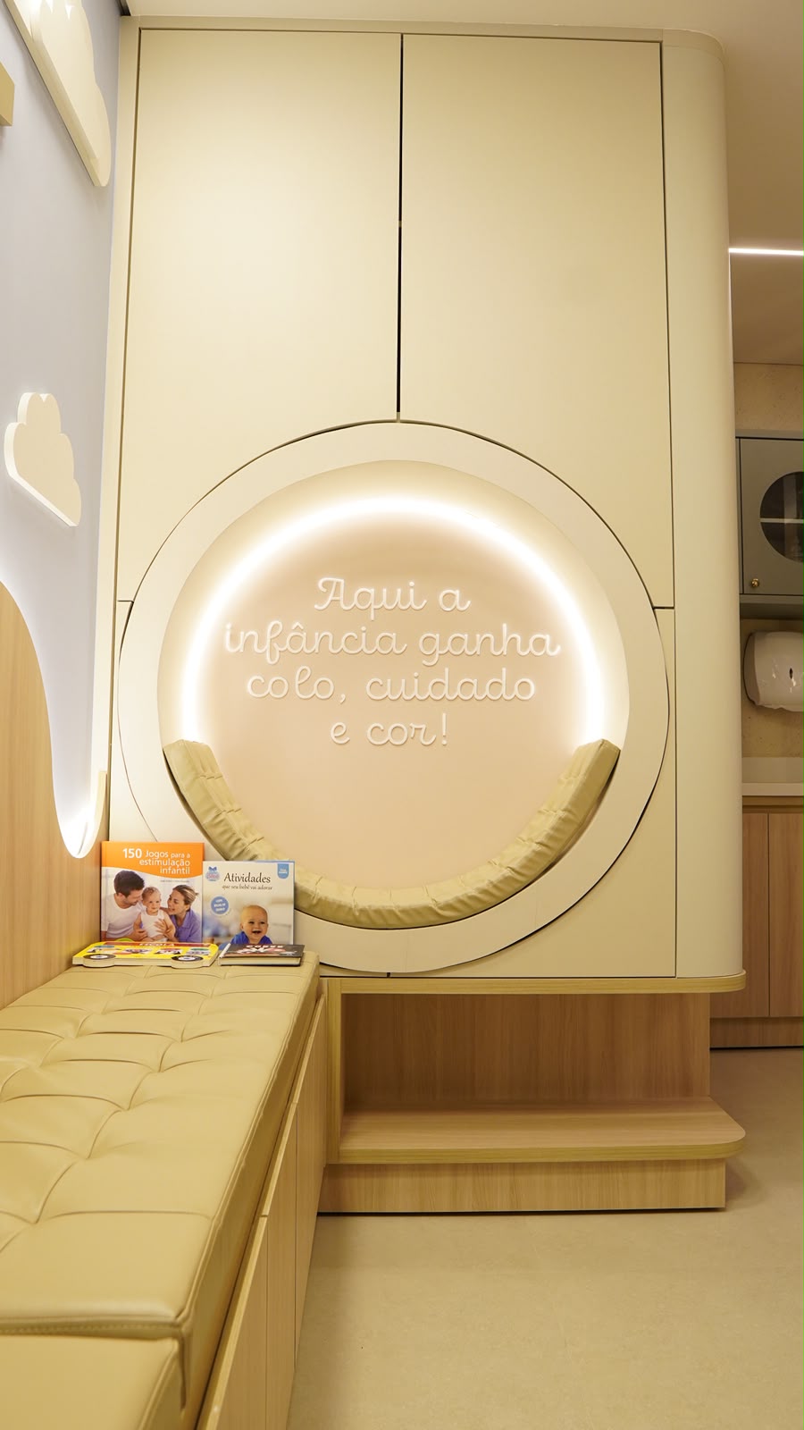 Cantinho de espera com um nicho aconchegante e a frase “Aqui a infância ganha colo, cuidado e cor!”