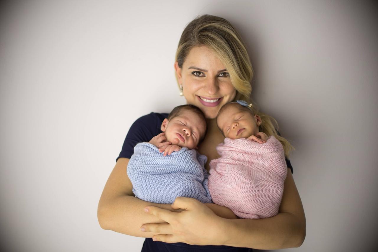 Dra. Halana Moura sorrindo com seus filhos gêmeos recém-nascidos no colo